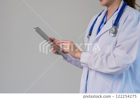 Confident Asian female doctor Standing and checking patient information on a tablet in the clinic. Confident Asian female doctor Standing and checking patient information on a tablet in the clinic. 122254275