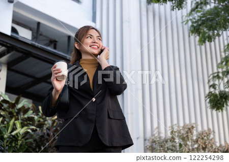 Confident Businesswoman Walking and Talking on Phone in Urban Cityscape with Coffee Confident Businesswoman Walking and Talking on Phone in Urban Cityscape with Coffee 122254298