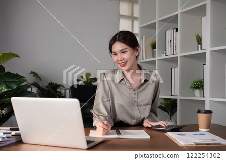 Young Asian business woman sitting in the office using a calculator to calculate business numbers. Young Asian business woman sitting in the office using a calculator to calculate business numbers. 122254302