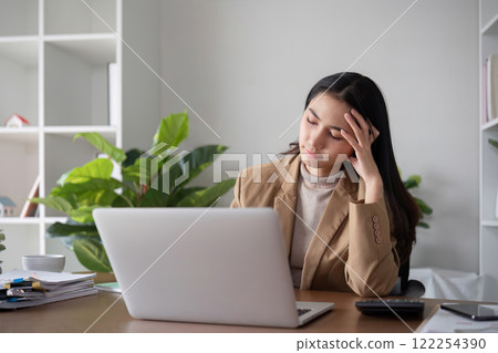 Unhappy Asian business woman shows stress over unsuccessful business while working in home office decorated with soothing green plants. 122254390