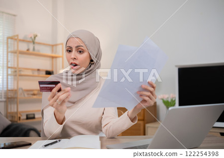 A young Muslim woman is shocked by an excessive bill from an online purchase made with a credit card through an online banking application. A young Muslim woman is shocked by an excessive bill from an online purchase made with a credit card through an online banking application. 122254398