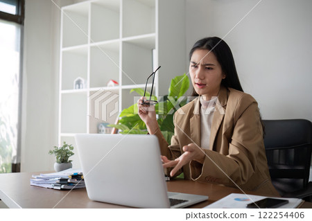 Asian businesswoman feeling tired and stressed over an unsuccessful business while working in a home office decorated with soothing green plants. 122254406