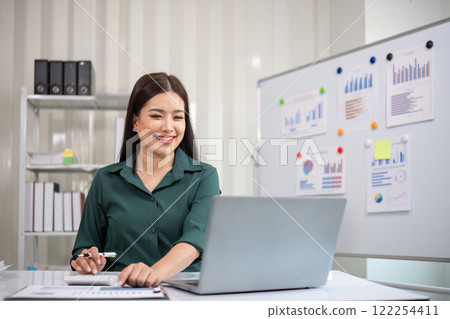 Beautiful determined business woman working using laptop and calculator calculating turnover in modern office Beautiful determined business woman working using laptop and calculator calculating turnover in modern office 122254411