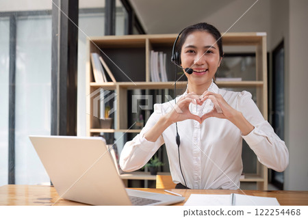 Call center operator makes heart-shaped hand gesture Wear headphones to talk to customers. Provide consultation via online channels on laptops 122254468
