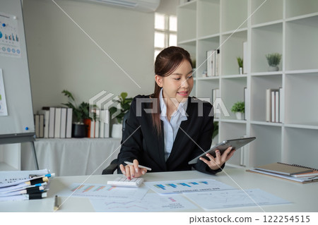 Young woman accountant uses calculator to calculate finances or graph business numbers on white wooden table in office. 122254515