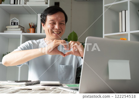 Caring professional creating a heart gesture on video call to express love from home office Caring professional creating a heart gesture on video call to express love from home office 122254518