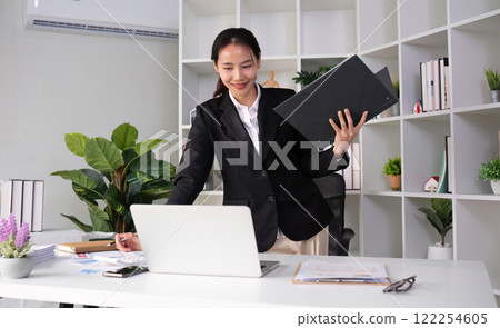 Young Asian business woman in a suit is checking work on her desk in the office. Young Asian business woman in a suit is checking work on her desk in the office. 122254605