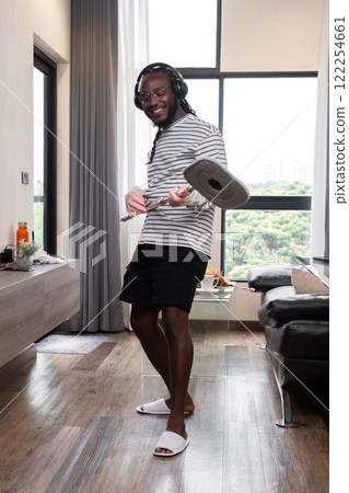 Happy young African American man doing housework, mopping floors, cleaning rooms on holiday, enjoying. 122254661