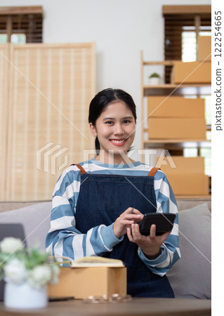 A young Asian entrepreneur sells product online through an online platform and pack product into shipping boxes. A young Asian entrepreneur sells product online through an online platform and pack product into shipping boxes. 122254665