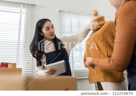 Fashion entrepreneur demonstrating sweater details to a colleague while planning a shirt launch in their boutique 122254674