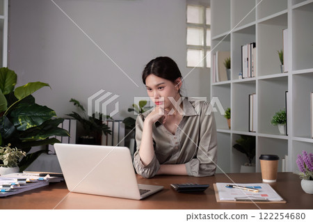 Unhappy Asian businesswoman shows stress while working in a home office decorated with soothing green plants. 122254680