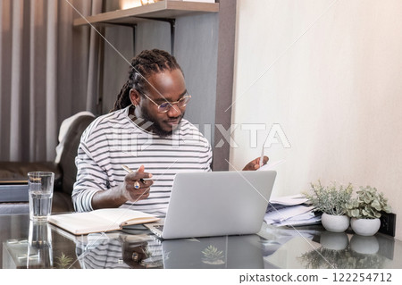 Young African American businessman spends his free time working from home on his laptop. Young African American businessman spends his free time working from home on his laptop. 122254712