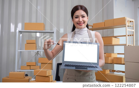 A small SME business owner stands holding a laptop with a white screen. Use a laptop to record small business information in your home office. A small SME business owner stands holding a laptop with a white screen. Use a laptop to record small business information in your home office. 122254807