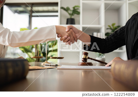A lawyer and a businesswoman shake hands and reach an agreement on a cooperation contract document. In the lawyer's office and there is a hammer lying on the table. 122254809