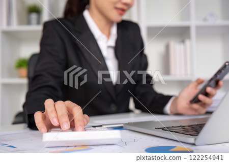Asian female accountant Use a calculator to calculate business numbers on a white wooden table in the office. 122254941