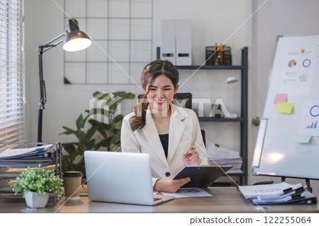 Asian businesswoman or accountant happily sitting and working with laptop on finance and business administration. On the desk in the office decorated with green plants. 122255064