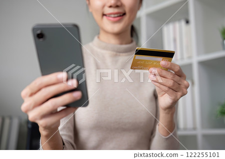 Beautiful young woman uses laptop to shop online, buys things and pays with credit card through phone online banking app. 122255101