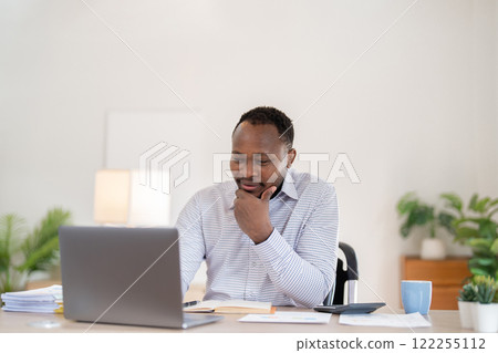 African American businessman working with laptop Take notes on documents in the office and prepare performance analysis reports. 122255112