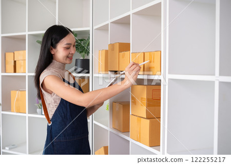 A small SME business owner receives product orders and writes shipping information on cardboard boxes in the home office to prepare for delivery. A small SME business owner receives product orders and writes shipping information on cardboard boxes in the home office to prepare for delivery. 122255217