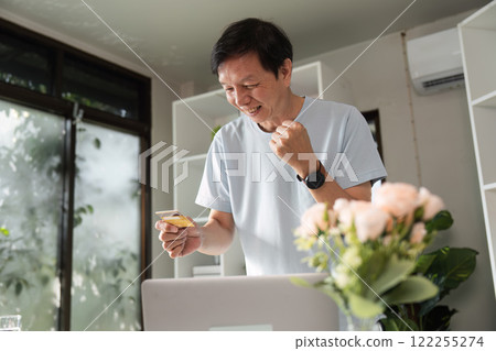 Joyful middle-aged man celebrating successful online shopping in his stylish home office Joyful middle-aged man celebrating successful online shopping in his stylish home office 122255274
