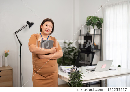 Confident Business Woman Standing in Modern Office with Tablet and Laptop, Embracing Success and Leadership Confident Business Woman Standing in Modern Office with Tablet and Laptop, Embracing Success and Leadership 122255317