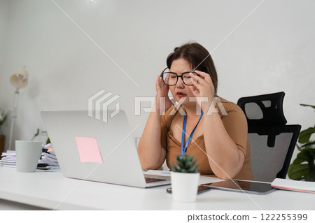 Stressed Businesswoman at Work Desk with Laptop and Papers in Modern Office Environment Stressed Businesswoman at Work Desk with Laptop and Papers in Modern Office Environment 122255399