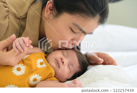 Asian mother kissing her newborn baby girl on white bed at home 122257439