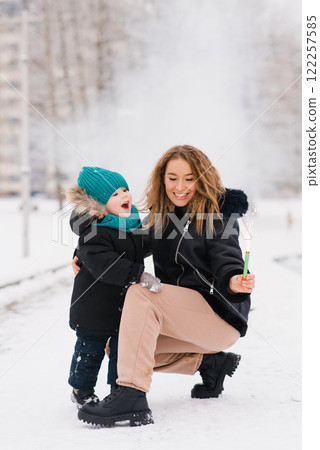 Happy mother and son rejoice at a lit sparkler in their hands in the snow 122257585