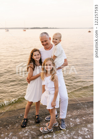 Family of four posing for picture on beach. The father is holding his two children while the other two children are standing next to him 122257593