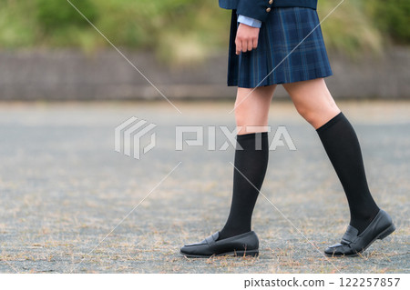 The feet of a female student in a blazer walking through a schoolyard or ground 122257857