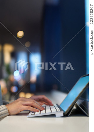 Hands typing on a computer keyboard in a space with a night view Hands typing on a computer keyboard in a space with a night view 122258267
