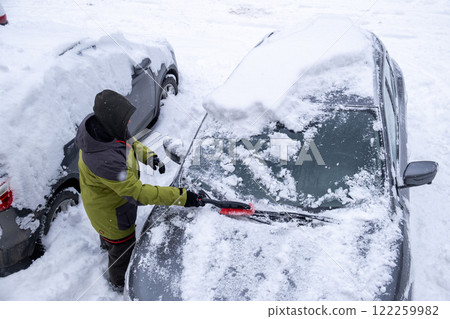 Person Clearing Snow from Car in Winter Landscape 122259982
