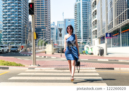 A slender woman crosses the road at a pedestrian crossing in a large city 122260020