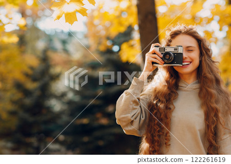 Smiling young woman with the photo camera shooting the forest trees with the yellow leaves at sunset 122261619