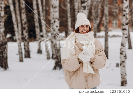 Happy smiling young woman portrait dressed coat scarf hat and mittens enjoys winter weather at birch winter park Happy smiling young woman portrait dressed coat scarf hat and mittens enjoys winter weather at birch winter park 122261630
