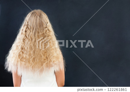 Back of young female model with long curly healthy hair on black background. Blond hair girl. Back of young female model with long curly healthy hair on black background. Blond hair girl. 122261861