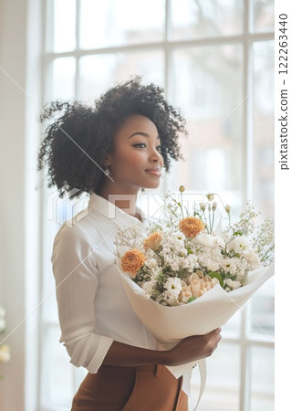 Beautiful young black woman, florist holding a bouquet, side view. For floral shop advertisements banner, greeting cards, vertical poster, Valentine's Day flyers, flower delivery. 122263440