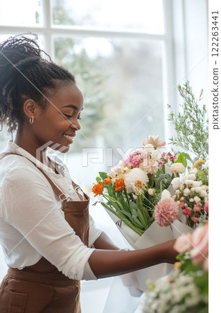 Beautiful black woman, smiling young florist holding a bouquet in a flower shop. For floral shop advertisements banner, greeting cards, vertical poster, Valentine's Day flyers, flower delivery. 122263441