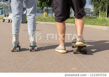 Young couple rollerblading and skateboarding in park. Happy and joyful girl and man doing sports together on warm summer day. High quality photo 122263516