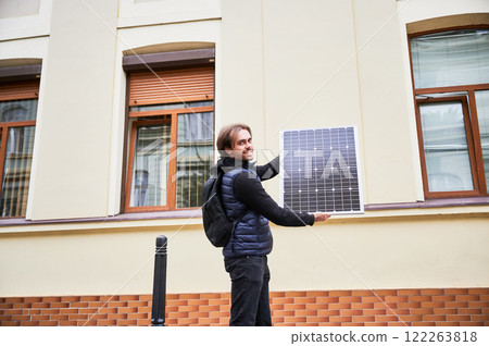 Man holding photovoltaic solar panel in front of historical building. Concept of integration of sustainable renewable energy sources into architecture. 122263818
