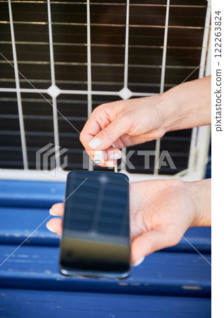 Close up view of woman charging her phone from solar battery. Young female using solar panel charger for mobile devices. Integration of sustainable renewable energy into everyday life. Close up view of woman charging her phone from solar battery. Young female using solar panel charger for mobile devices. Integration of sustainable renewable energy into everyday life. 122263824