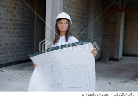 Female architect holding blueprint, inspecting construction site progress 122264143