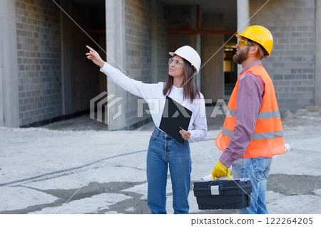 Female architect pointing at something while discussing with construction worker at building site 122264205