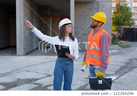 Female architect pointing at something while discussing with construction worker at building site Female architect pointing at something while discussing with construction worker at building site 122264206