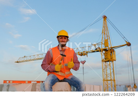 Construction worker sitting and holding hammer at construction site 122264209