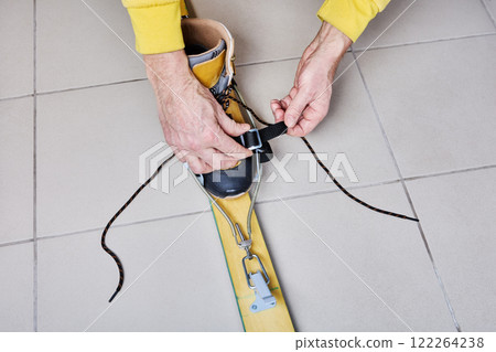 Adjusting universal cable ski bindings to fit trekking boot, tightening strap on bracket. 122264238