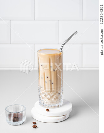 Cold latte coffee in a tall glass with milk and straw on a light table on a white brick background 122264391
