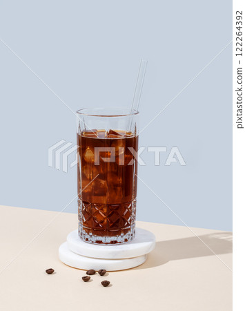 Cold brew coffee in a tall glass with ice and straw on a marble stand on a yellow-blue background Cold brew coffee in a tall glass with ice and straw on a marble stand on a yellow-blue background 122264392