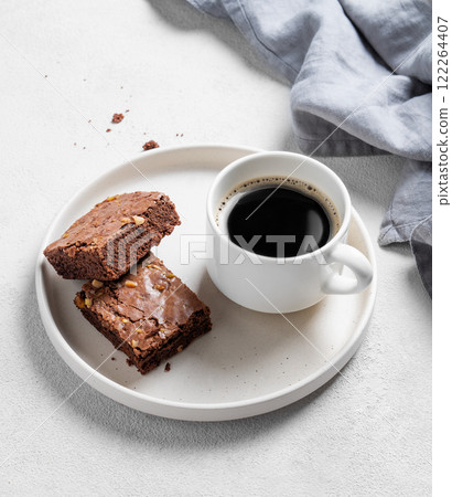 Pieces of chocolate brownie with nuts on a plate with a cup of espresso coffee on a light background 122264407