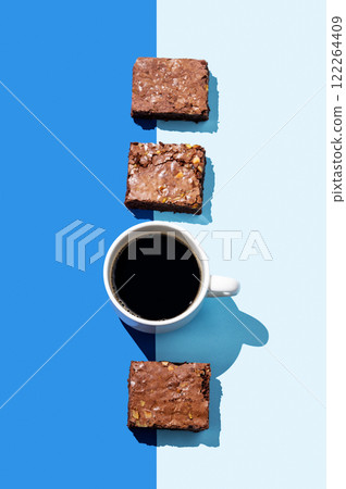 Pieces of chocolate brownie and a cup of espresso coffee on a blue background with hard light. 122264409